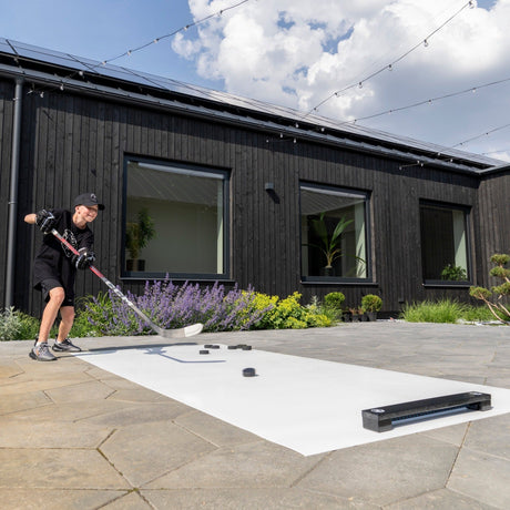 Hockey player passing with a rebounder on training tiles in a backyard — two-player drill setup