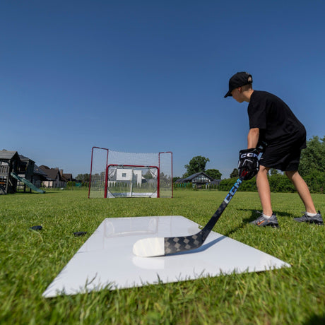Hockey player winding up for a shot from a shooting pad in the backyard with a net in the background