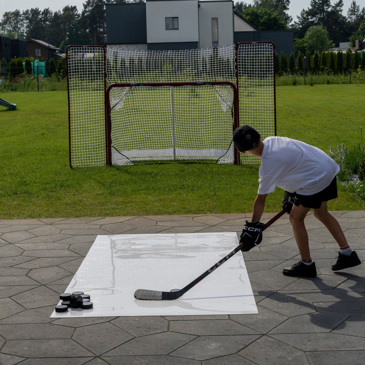 Young hockey player taking a shot on a roll-up shooting pad in the backyard toward a net
