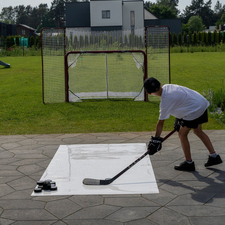 Young player practicing hockey shooting at home from a roll-up shooting pad toward a net with backstop