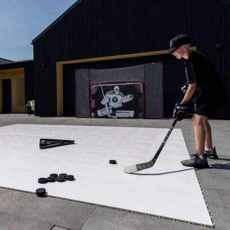 Young hockey player shooting on flooring tiles toward a goal in the driveway