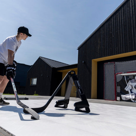 Teenage hockey player stickhandling around the Pro Defender in a backyard setting with a hockey net visible in the background