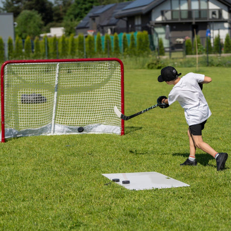Young child shooting a hockey puck on a training pad in the backyard toward a net