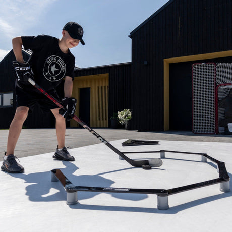 Young hockey player training stickhandling skills outdoors with a Better Hockey trainer setup