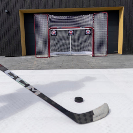 Hockey stick and puck on a shooting surface in front of a net with shooting targets installed in the corners