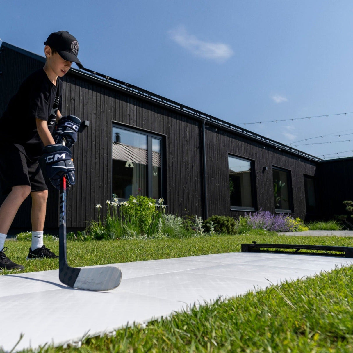 Ung pojke tränar hockey på Extreme Hockey Flooring Tiles utomhus, med hus och grönska i bakgrunden.