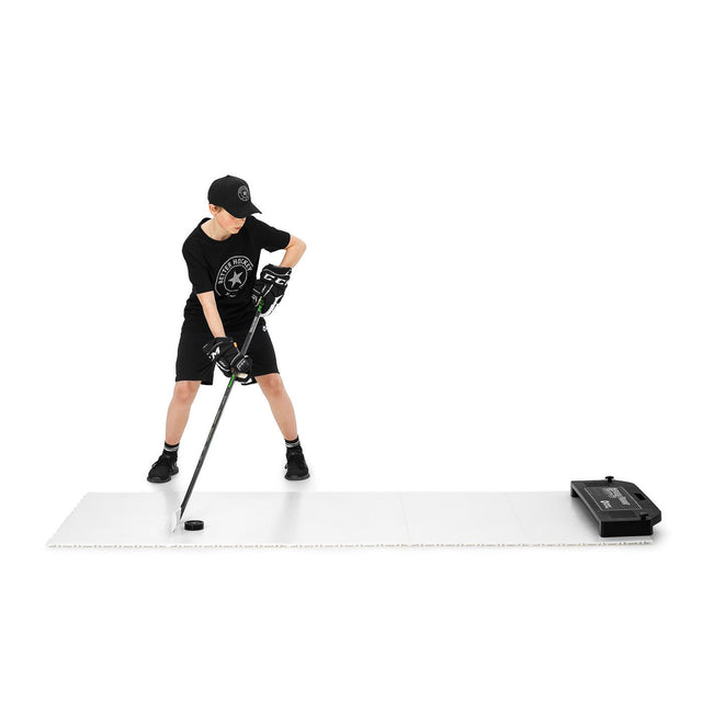 Ung kille tränar passningar med hockeyklubba och puck på Extreme Hockey Flooring Tiles Passing Kit, perfekt för skottramp och hockeymål.